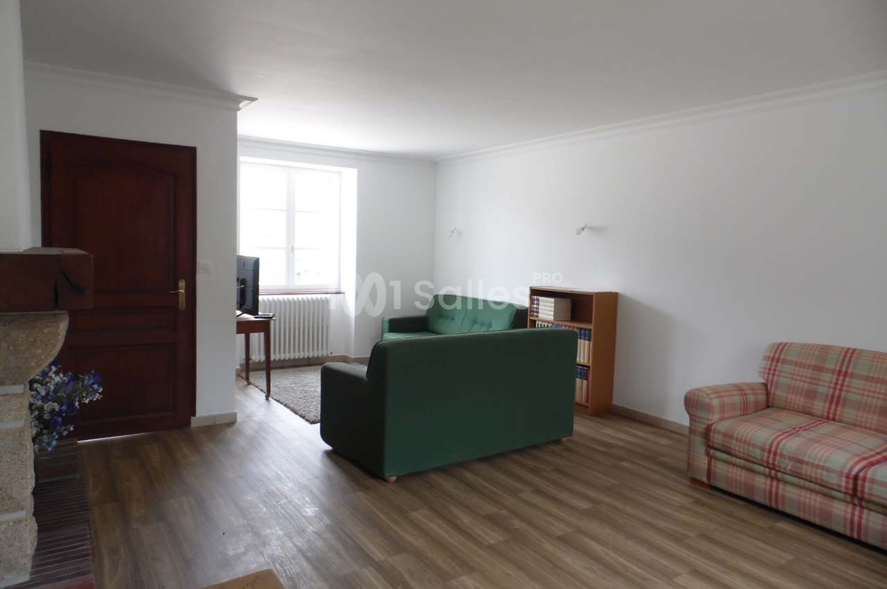 Salon lumineux avec parquet, canapé vert, fauteuil à carreaux, étagère en bois et fenêtre laissant entrer la lumière…