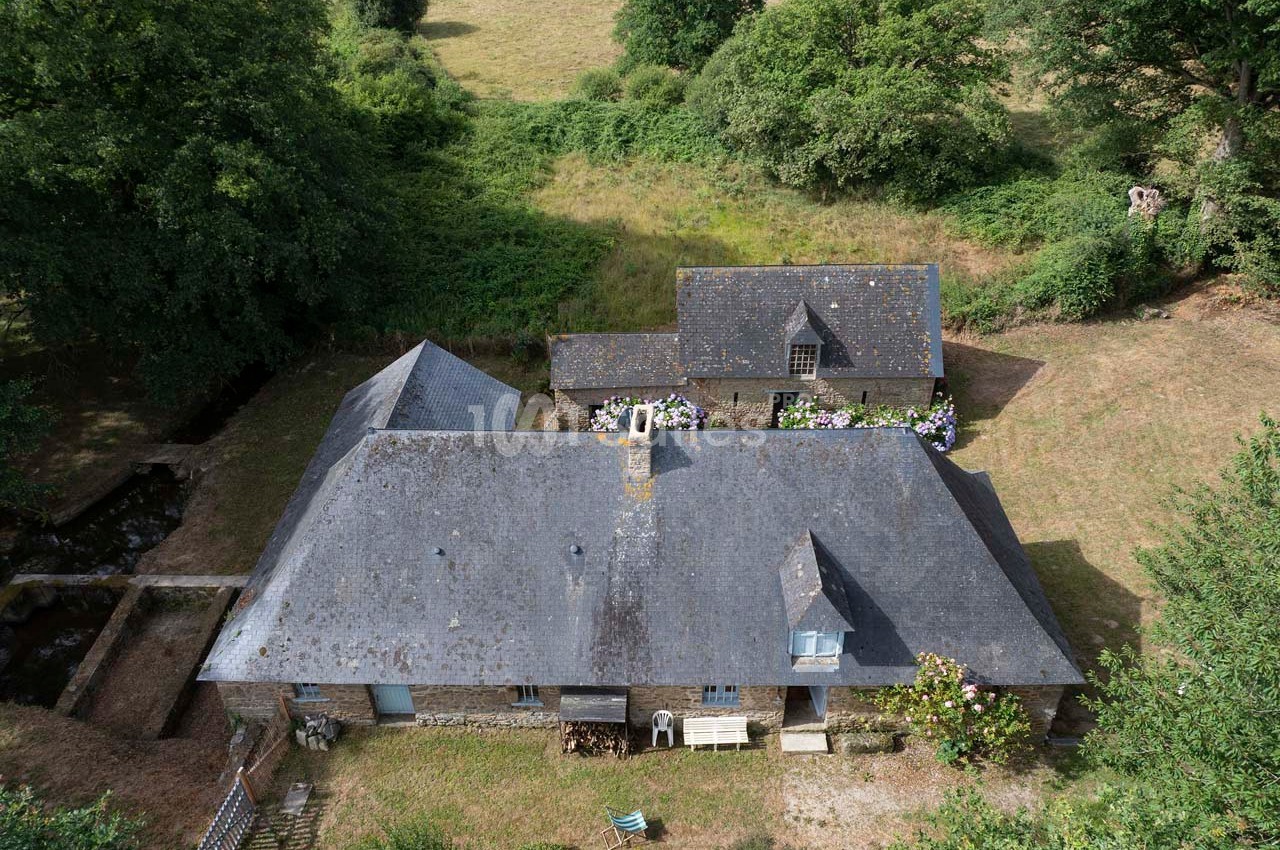 Vue aérienne d'une maison en pierre avec toit en ardoise, entourée de verdure et de champs.