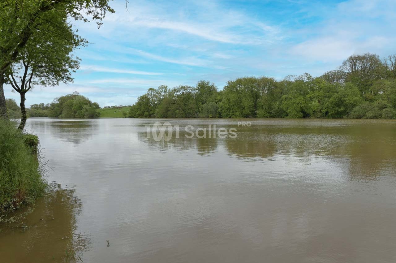 Vue d'un lac calme entouré d'arbres et de verdure sous un ciel partiellement nuageux.