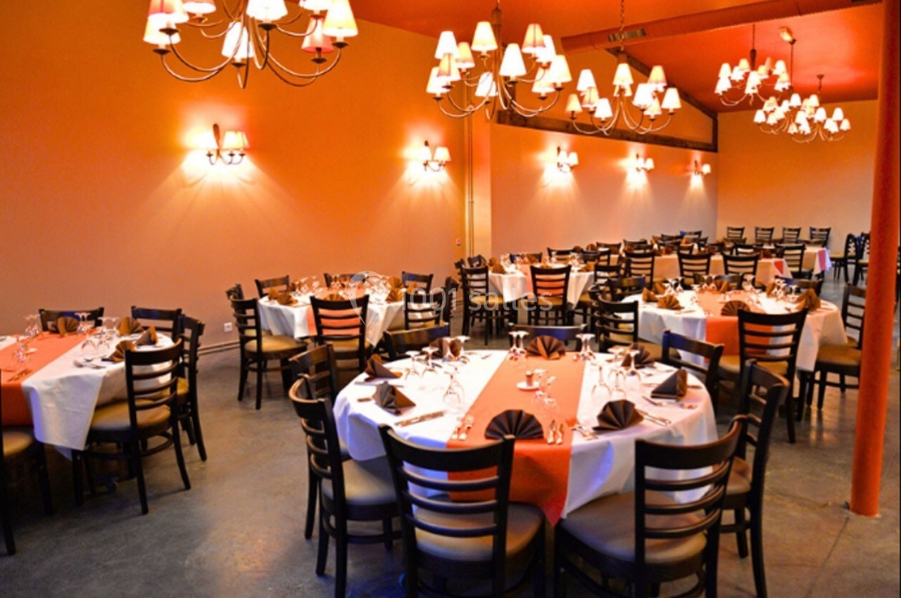 Salle de réception avec tables rondes dressées, nappes colorées et éclairage chaleureux par des lustres suspendus.