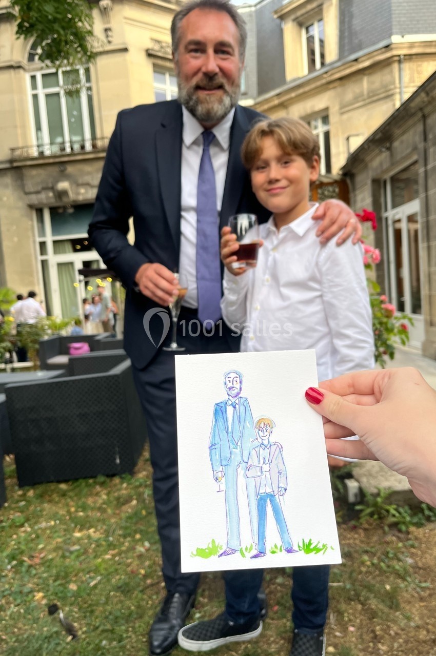 Un homme en costume et un enfant posent debout dans un jardin, une illustration d'eux est tenue au premier plan.