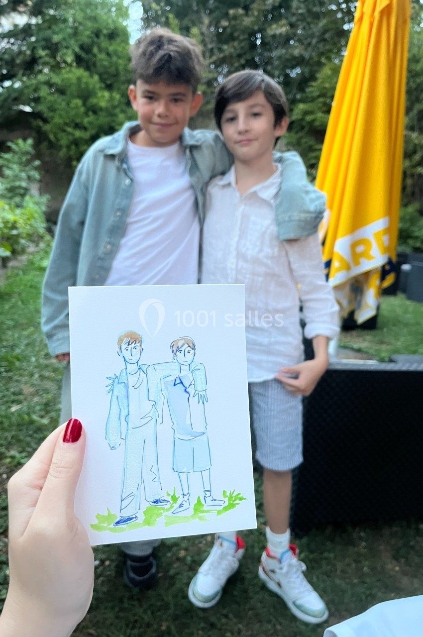 Deux enfants posent ensemble dans un jardin, une main tenant un dessin les représentant au premier plan.
