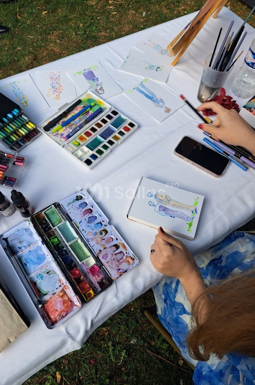 Une personne peint une illustration à l'aquarelle sur une table avec des fournitures artistiques et des croquis.