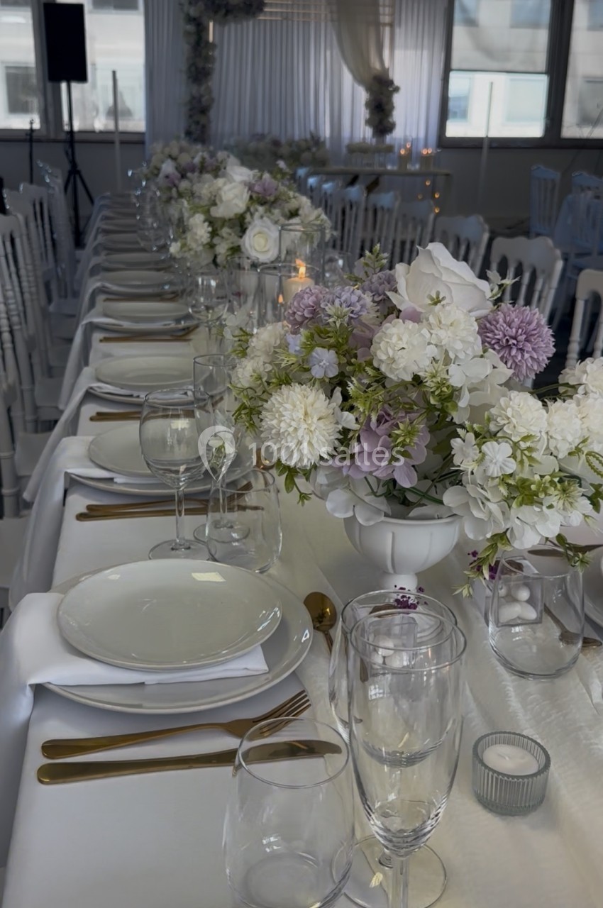 Table de réception élégamment dressée avec des assiettes blanches, couverts dorés et centres de table fleuris.