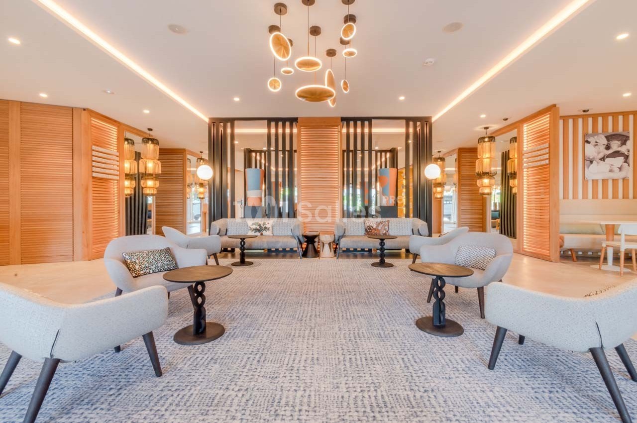 Salon moderne avec canapés clairs, tables basses noires, éclairage suspendu et décorations en bois et métal.
