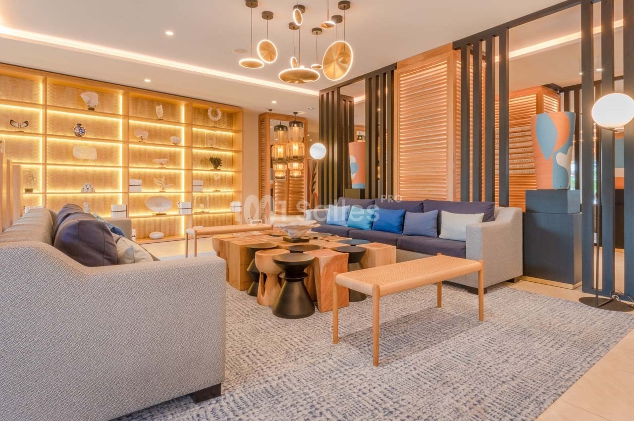 Salon moderne avec canapés, tables en bois, étagères éclairées et luminaires suspendus dans une ambiance chaleureuse.