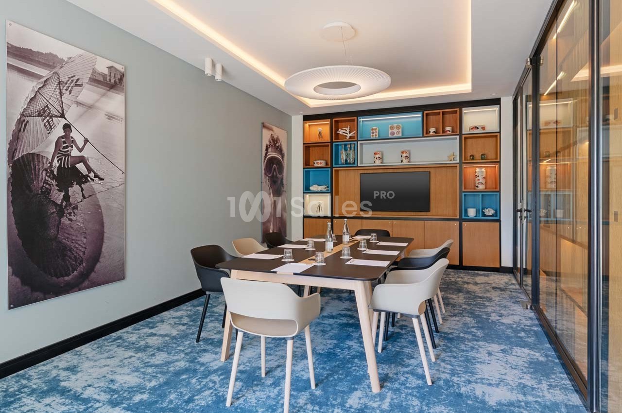 Salle de réunion moderne avec table, chaises, écran mural, étagères décoratives et éclairage intégré.