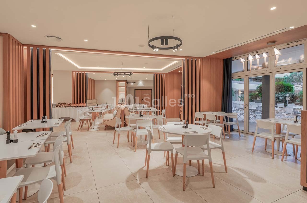 Salle de restaurant lumineuse avec des tables et chaises blanches, décor moderne en bois clair, vue sur une terrasse…