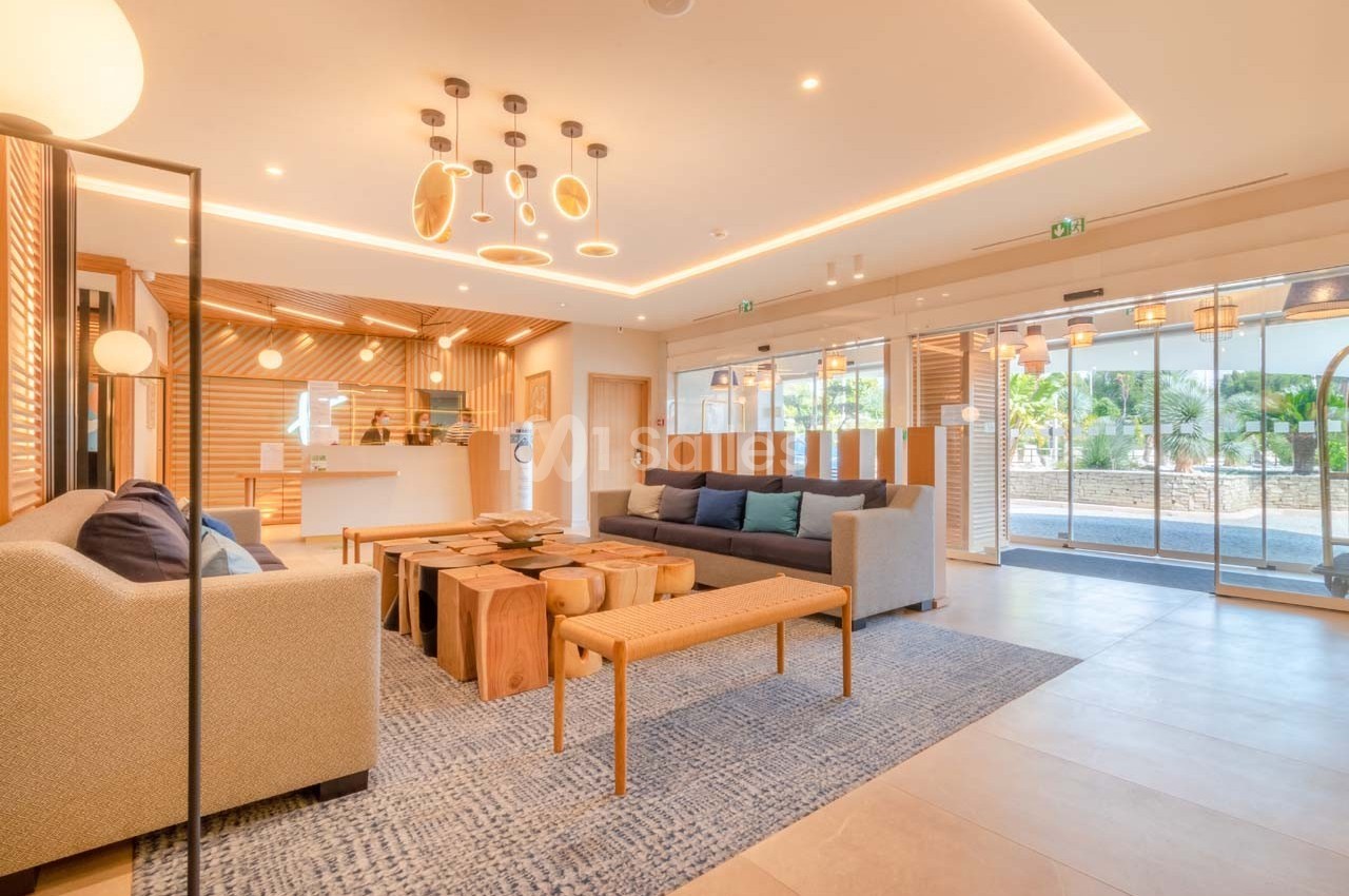 Salon moderne avec mobilier en bois, canapés, éclairage design et grandes baies vitrées donnant sur un espace extérieur.