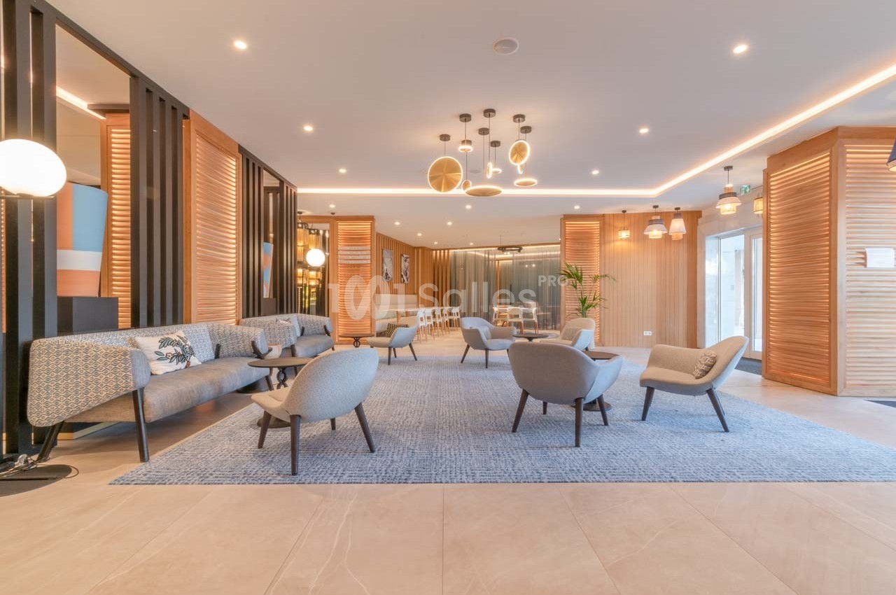 Espace lounge moderne avec fauteuils, canapés, tapis bleu et éclairage design dans un intérieur lumineux et chaleureux.