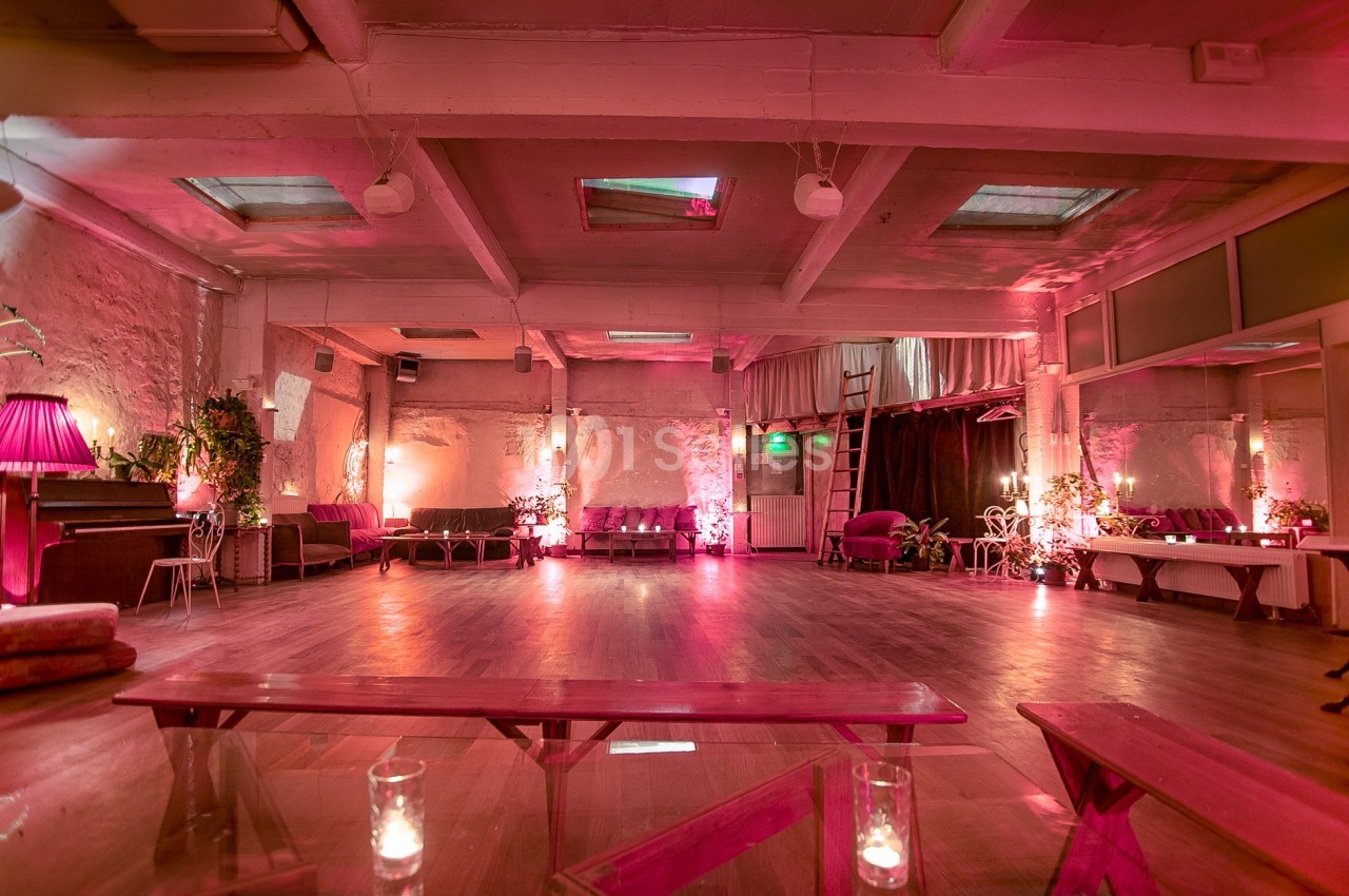 Salle spacieuse avec éclairage tamisé rose, mobilier vintage, plantes et parquet en bois.
