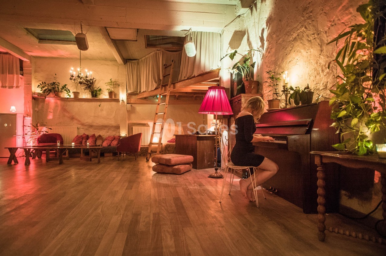 Une femme joue du piano dans une pièce chaleureuse éclairée par des lampes et décorée de plantes et de coussins.