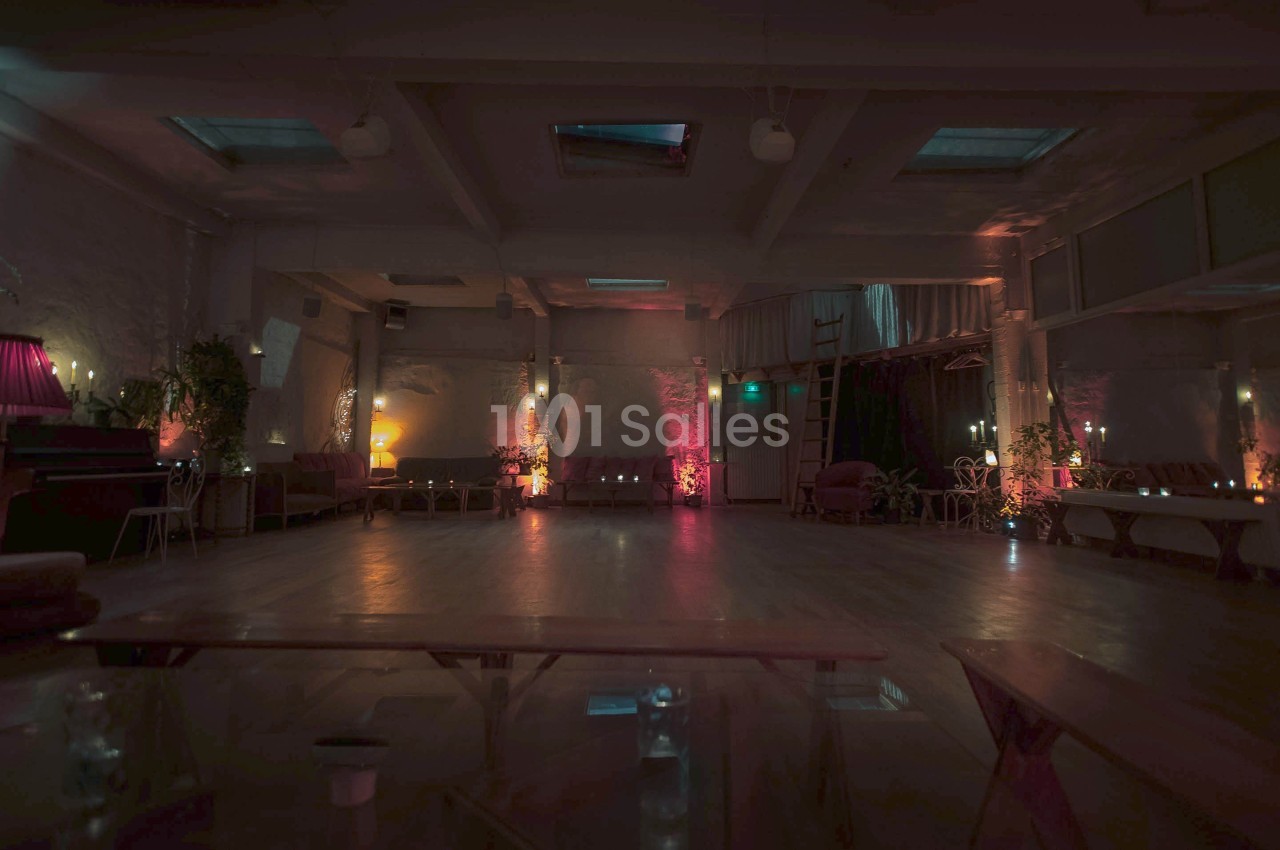 Salle spacieuse faiblement éclairée avec des lumières tamisées, des plantes et des sièges disposés le long des murs.