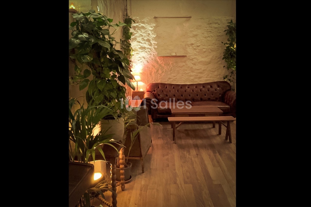 Canapé en cuir marron dans un salon cosy avec plantes vertes, murs en pierre et éclairage tamisé.