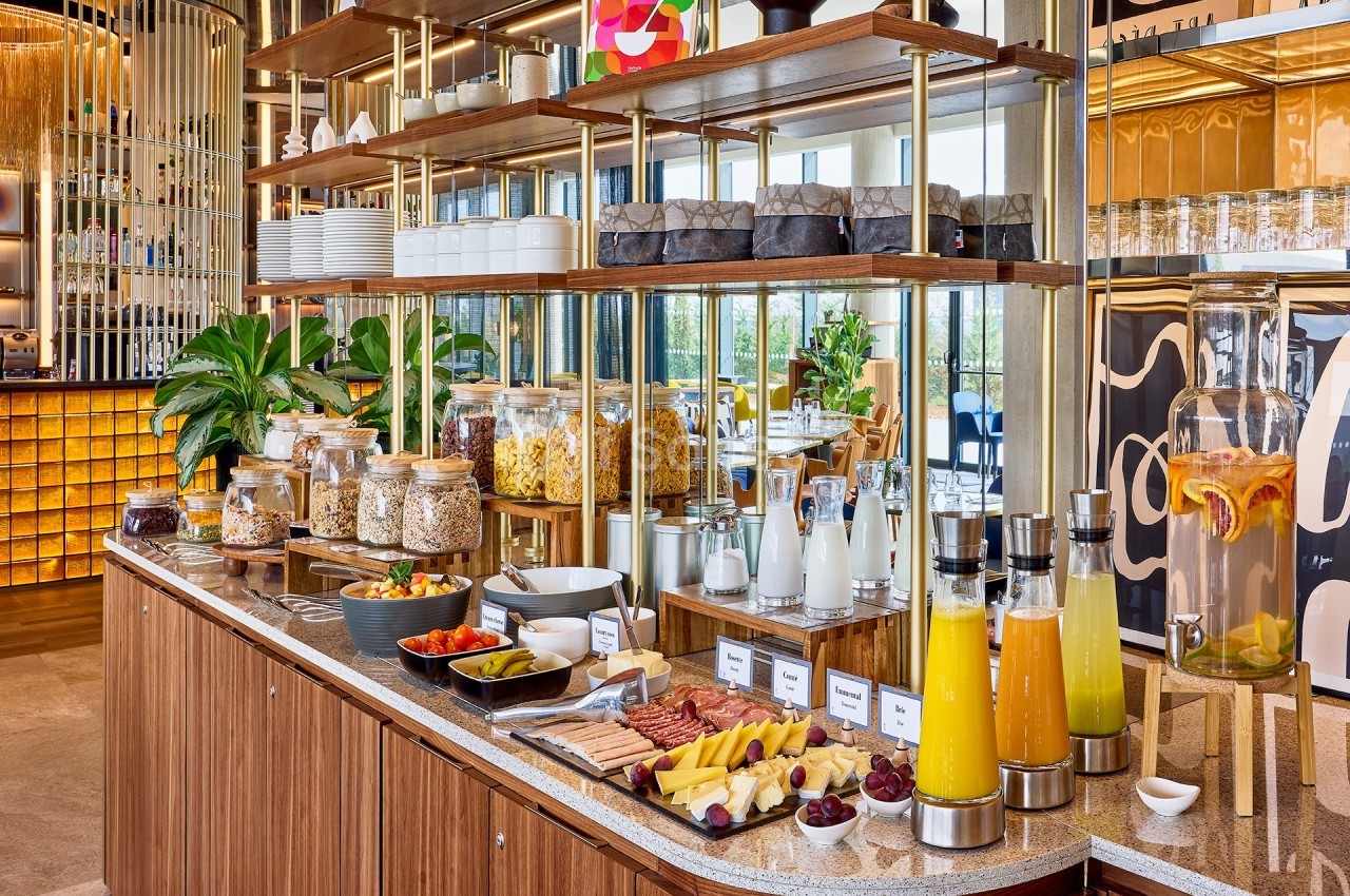 Buffet de petit-déjeuner avec fruits, céréales, jus, viennoiseries et autres aliments disposés sur un comptoir en bois.