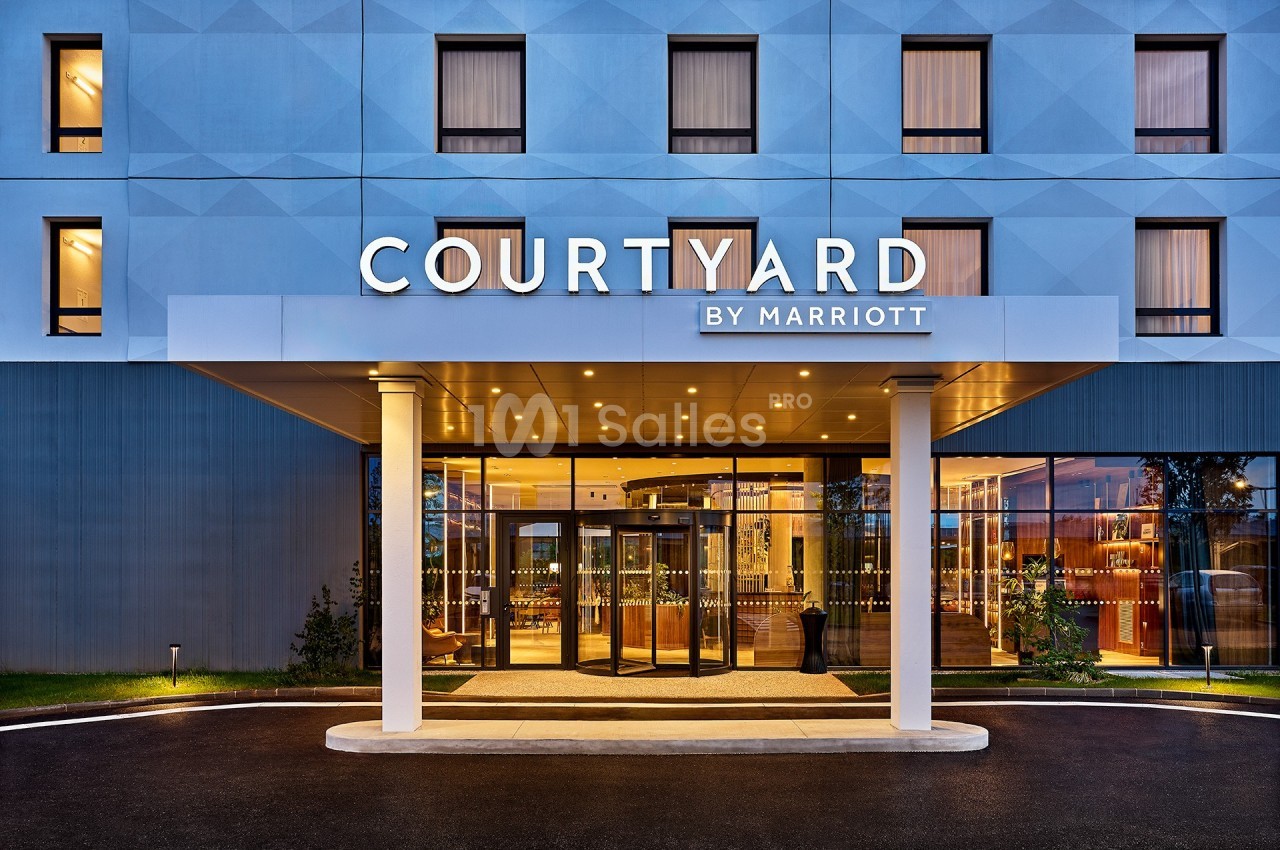 Façade d'un hôtel moderne avec enseigne ’Courtyard by Marriott’ et entrée éclairée sous un auvent.