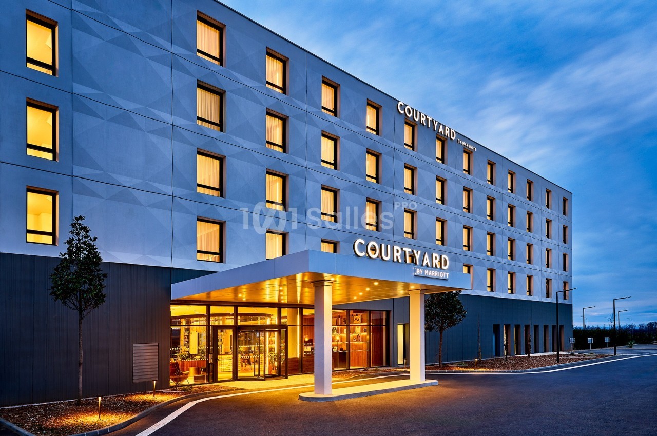 Façade d'un hôtel moderne éclairé au crépuscule, avec entrée principale vitrée et enseigne ’Courtyard’.