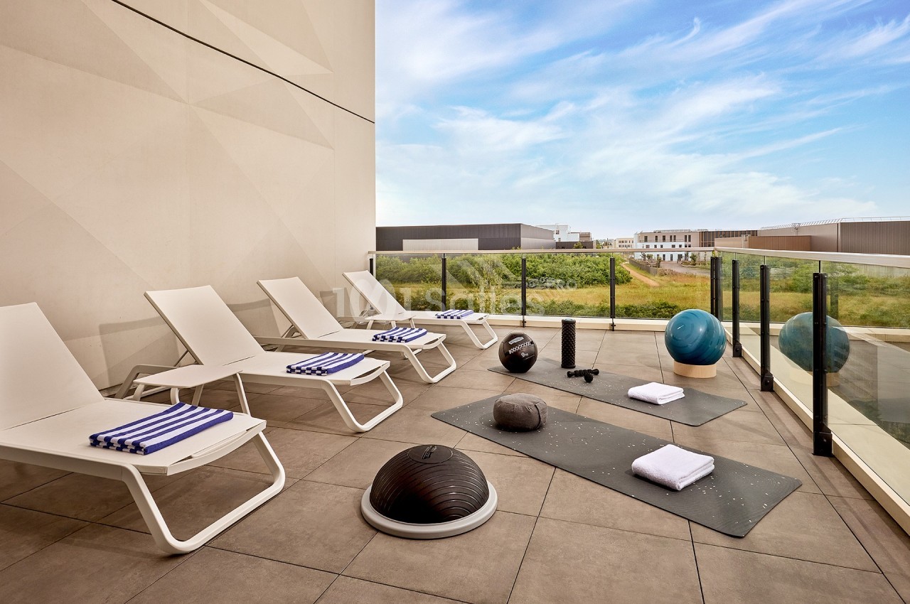 Terrasse avec chaises longues, tapis de sport, accessoires de fitness et vue sur un paysage dégagé.