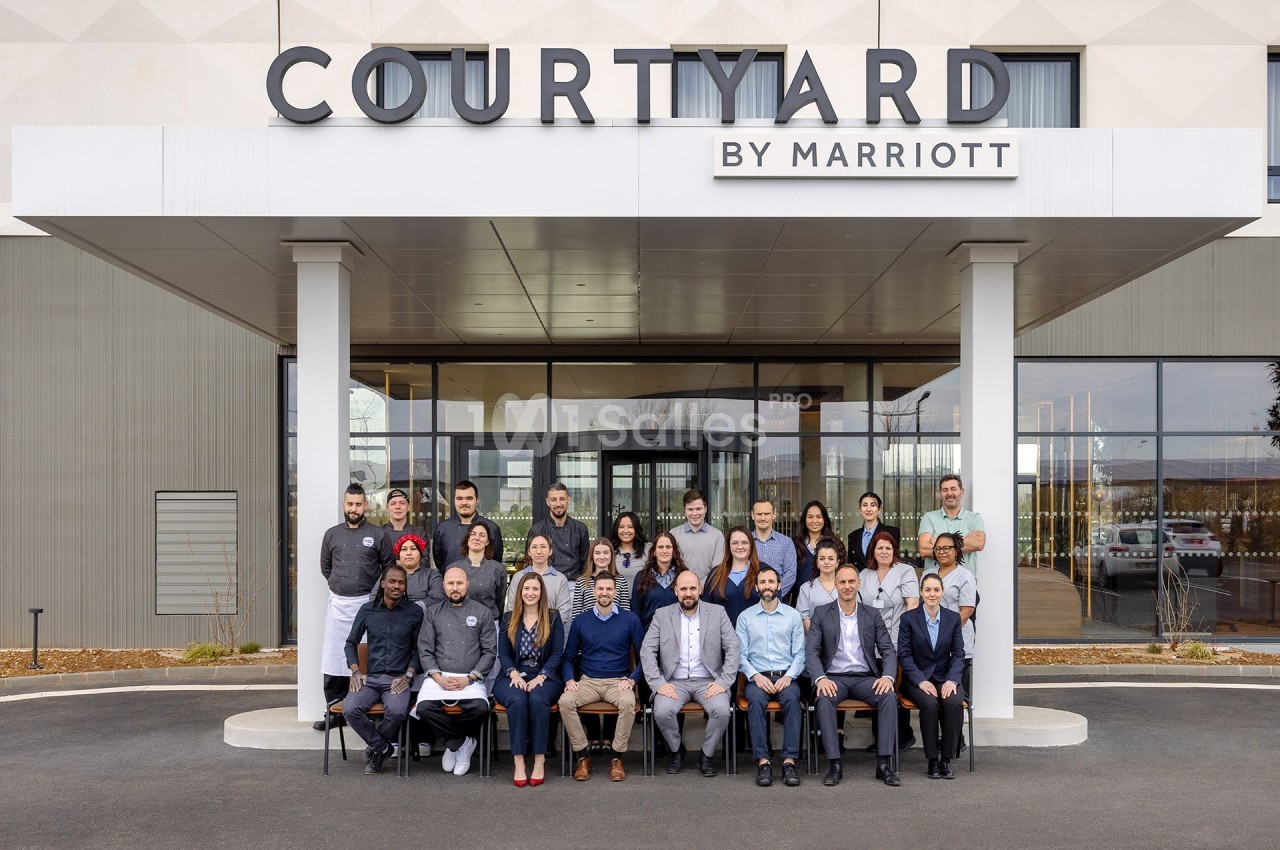 Photo de groupe devant l'entrée principale d'un hôtel Courtyard by Marriott, avec le logo visible au-dessus.