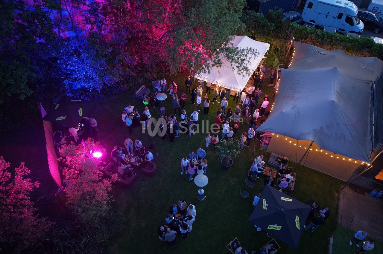 Vue aérienne d'une fête en plein air avec des tentes éclairées, des invités rassemblés et des lumières colorées.