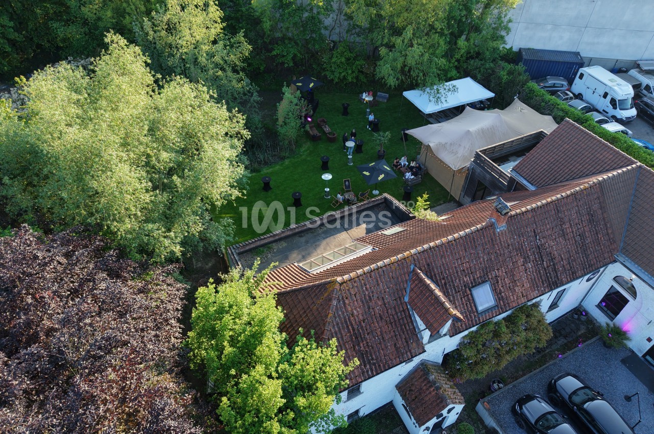 Vue aérienne d'une maison avec un jardin aménagé, des tables, des chaises et des arbres environnants.
