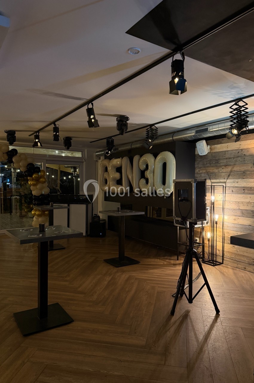 Salle décorée pour un événement avec ballons noirs et dorés, lettres ’GEN30’ illuminées et éclairage tamisé.