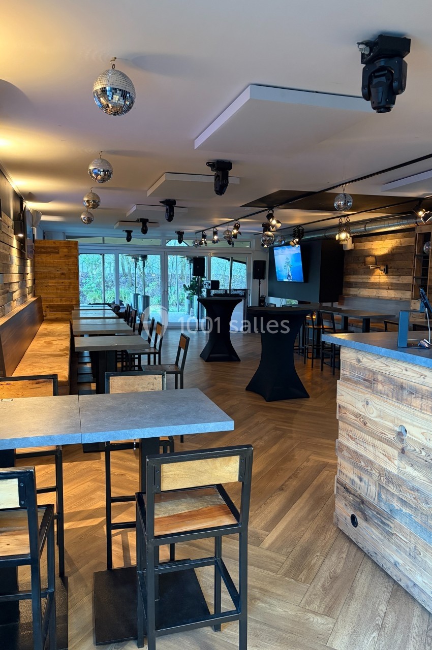 Salle moderne avec parquet, tables en bois, chaises hautes, bar en bois, éclairage suspendu et baies vitrées donnant sur l…