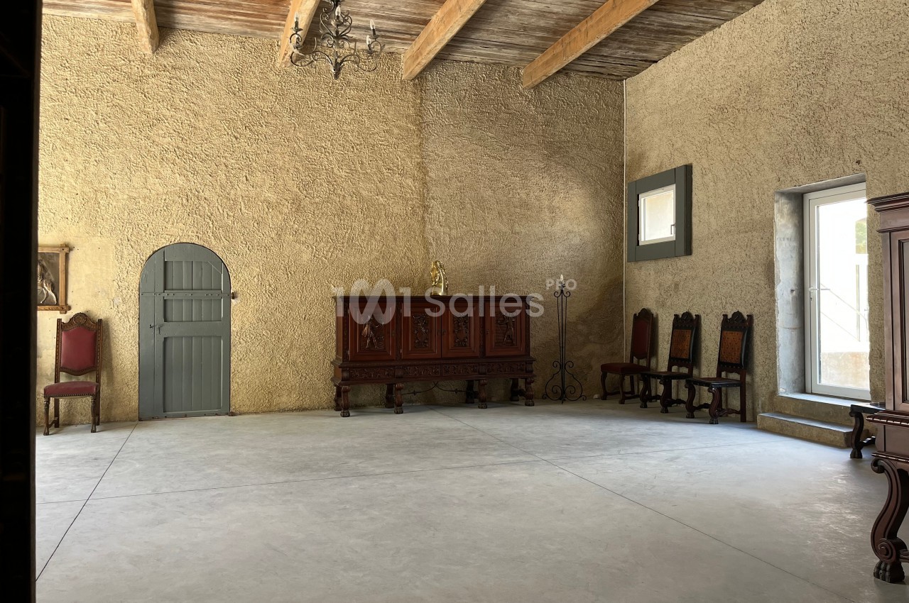 Salle avec murs en pierre beige, plafond en poutres apparentes, mobilier ancien en bois et lumière naturelle.