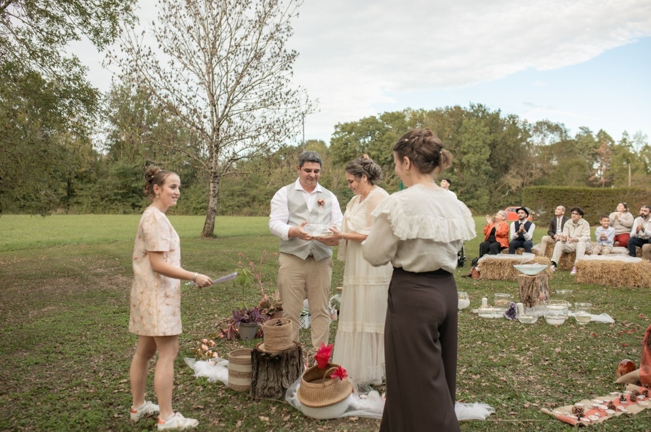 Cérémonie de mariage en plein air avec un couple échangeant des vœux entouré d'invités assis sur des bottes de foin.