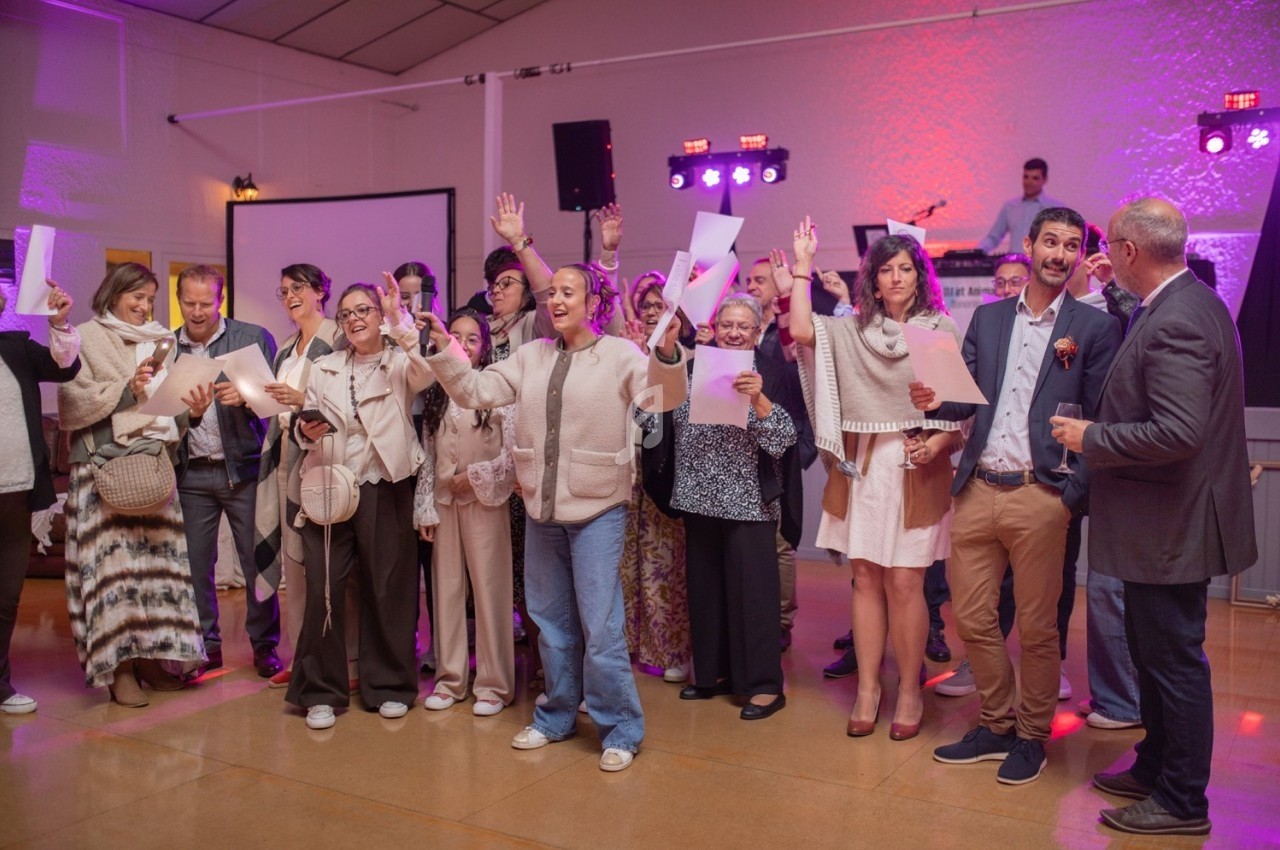 Un groupe de personnes debout dans une salle, certaines levant la main, avec un DJ en arrière-plan.
