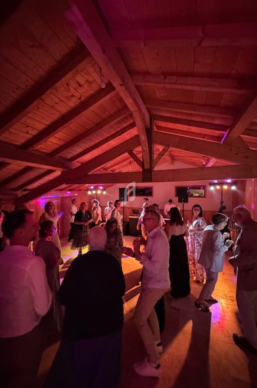 Des personnes dansent dans une salle en bois éclairée par des lumières colorées lors d'un événement festif.