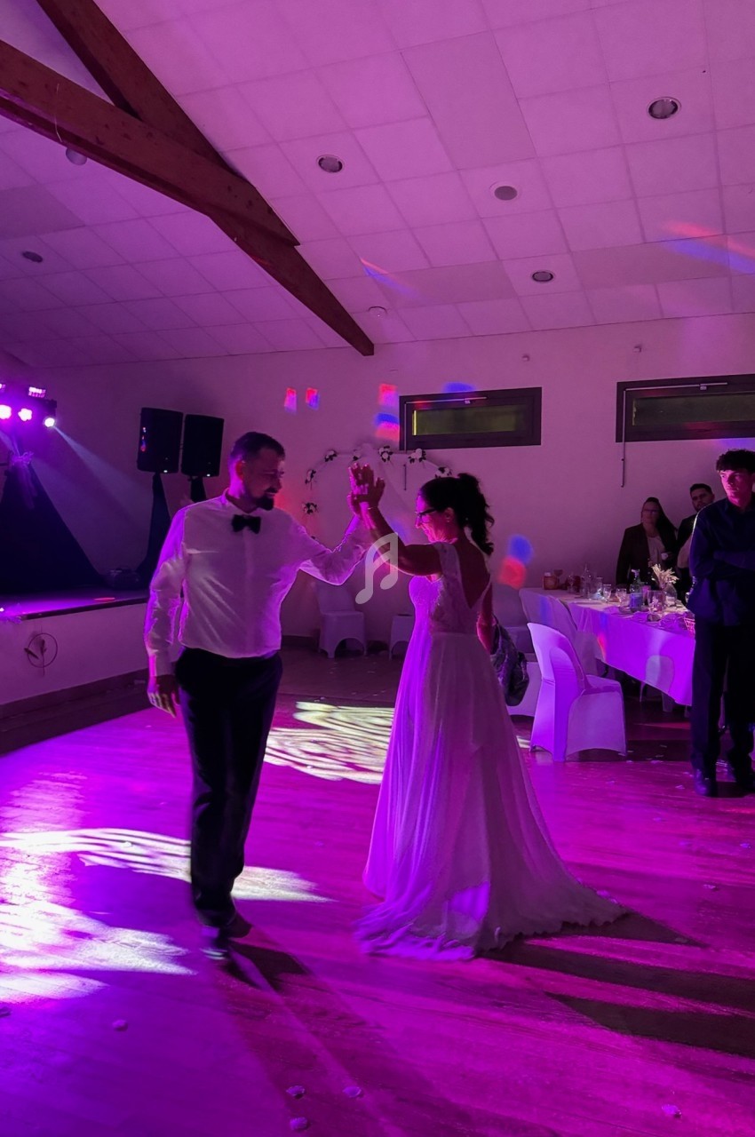 Un couple danse sous des lumières colorées dans une salle de réception avec des invités en arrière-plan.