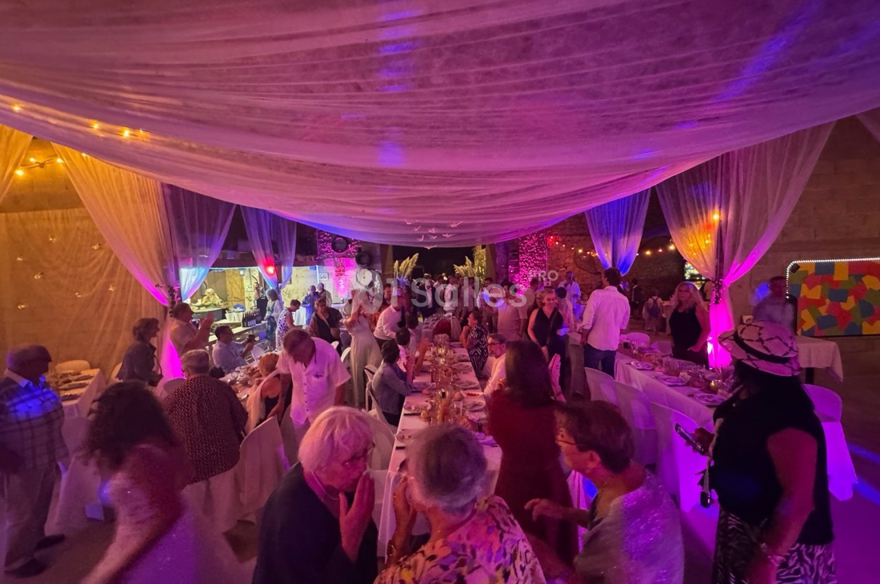 Salle décorée avec des voilages et éclairages colorés, remplie de personnes discutant autour de tables dressées.