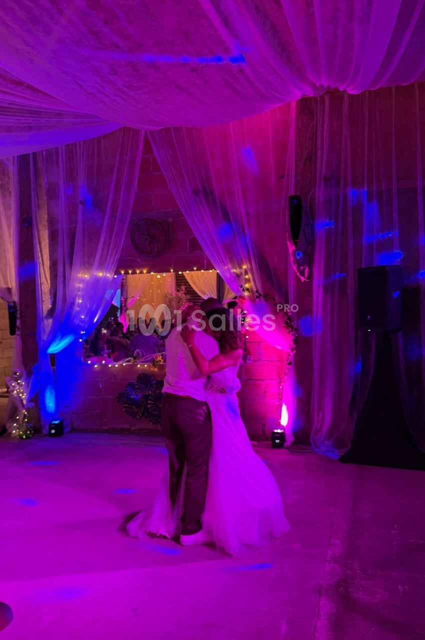 Un couple danse sous des lumières colorées dans une salle décorée de voilages et de guirlandes lumineuses.