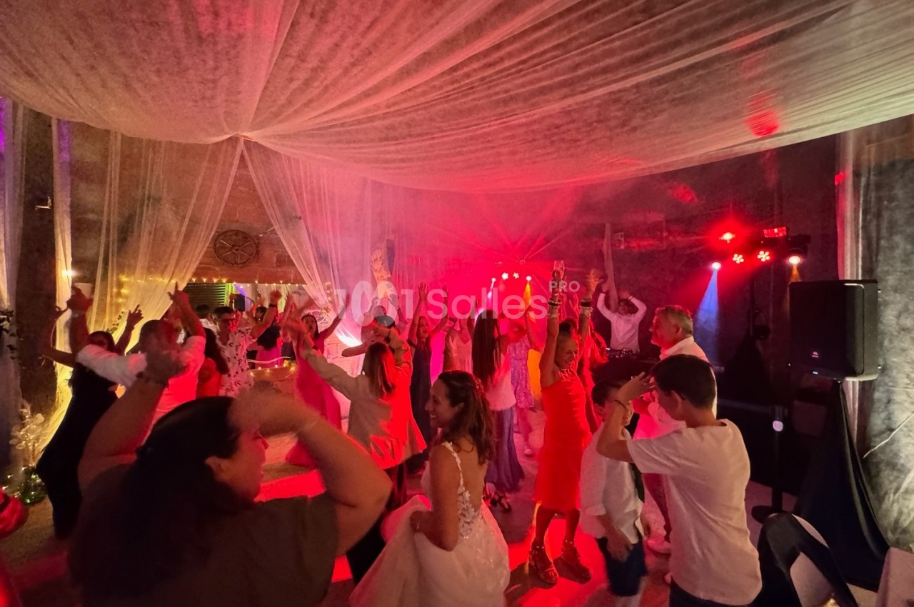 Groupe de personnes dansant sous un éclairage coloré dans une salle décorée avec des voilages suspendus.