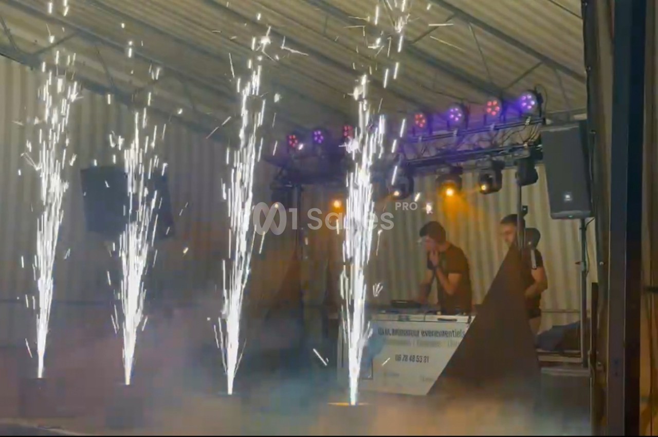 Effets pyrotechniques illuminant une scène avec des DJ en arrière-plan sous un chapiteau.