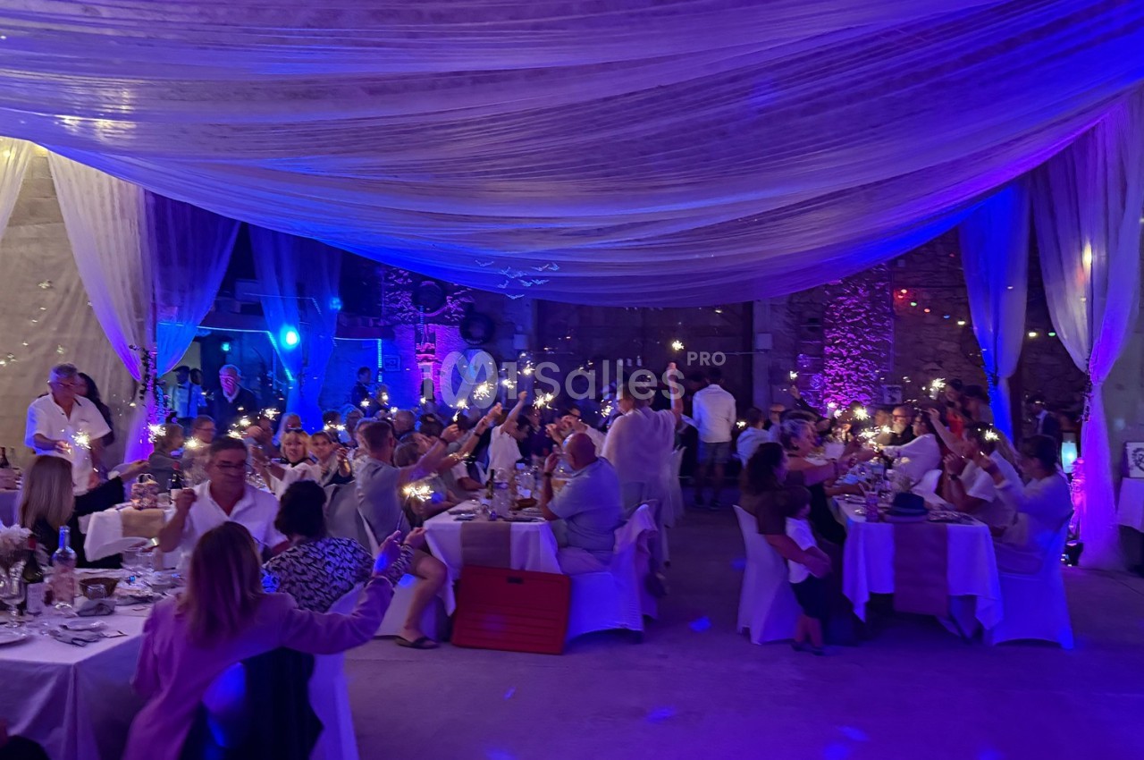 Des convives assis à des tables décorées, levant des lumières dans une salle éclairée par des lumières colorées et des…