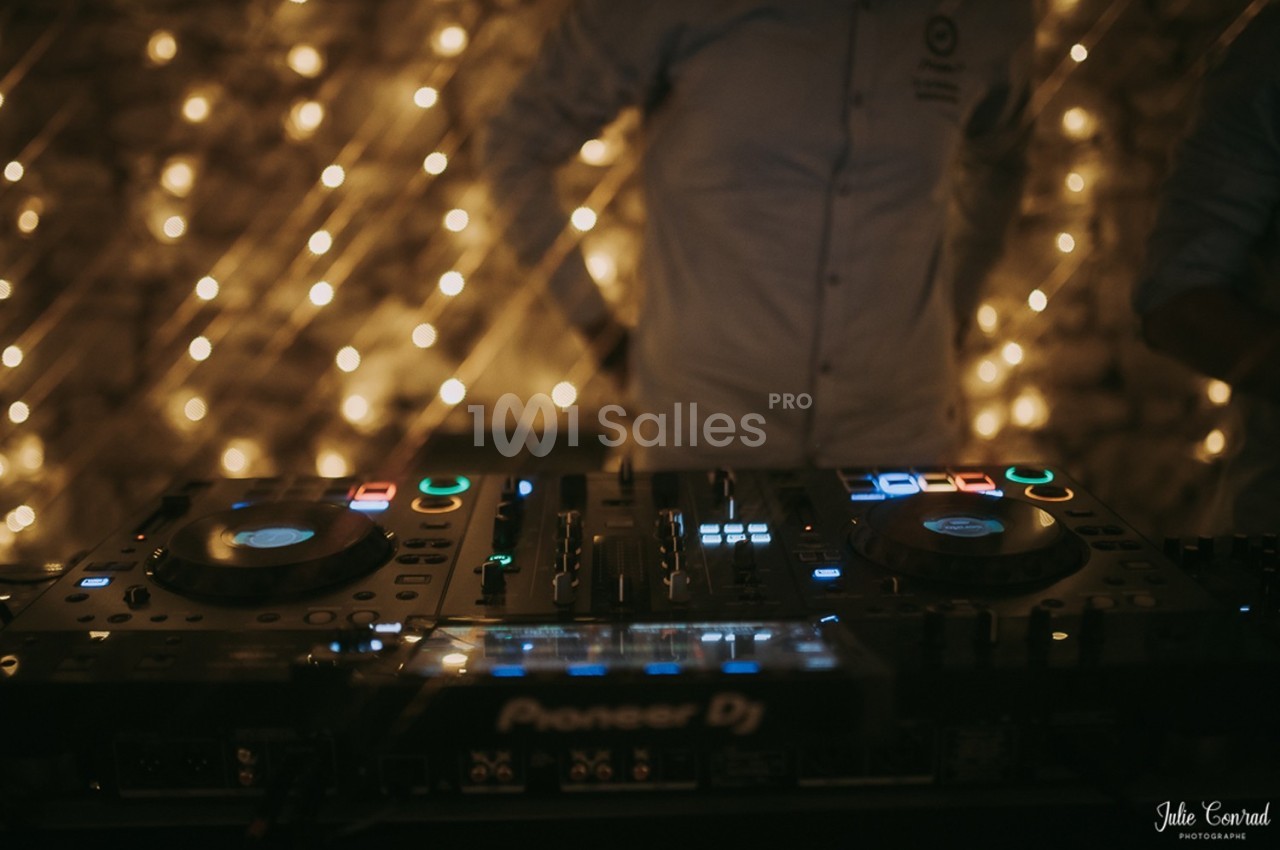 Console de mixage DJ éclairée, avec des lumières floues en arrière-plan dans une ambiance tamisée.