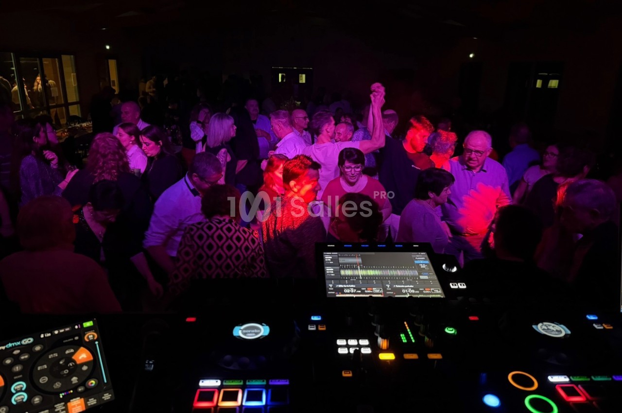 Groupe de personnes dansant dans une salle sombre, éclairée par des lumières colorées, vue depuis une table de mixage.