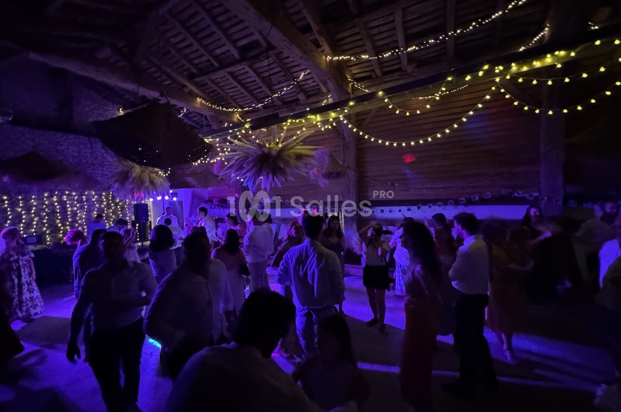 Personnes dansant sous des guirlandes lumineuses dans une salle aux murs en pierre et au plafond en bois.