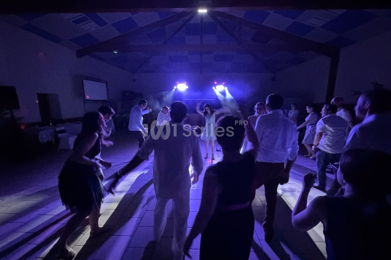 Personnes dansant sous des lumières colorées dans une salle sombre avec un plafond en poutres apparentes.