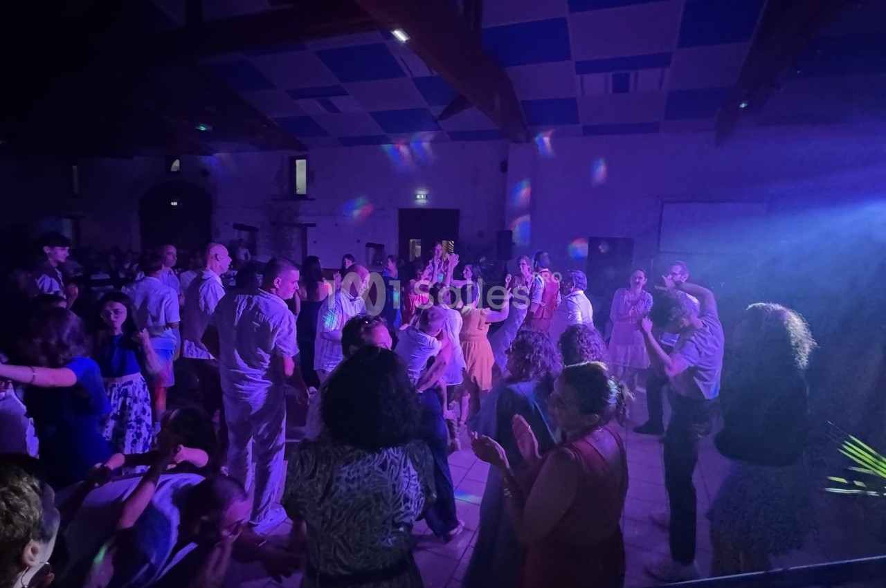 Groupe de personnes dansant dans une salle éclairée par des lumières colorées, ambiance festive en soirée.