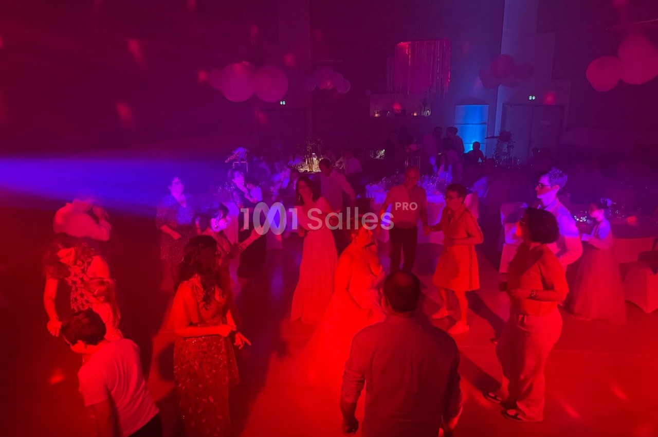 Personnes dansant dans une salle faiblement éclairée avec des lumières rouges et bleues, décorée pour une fête.