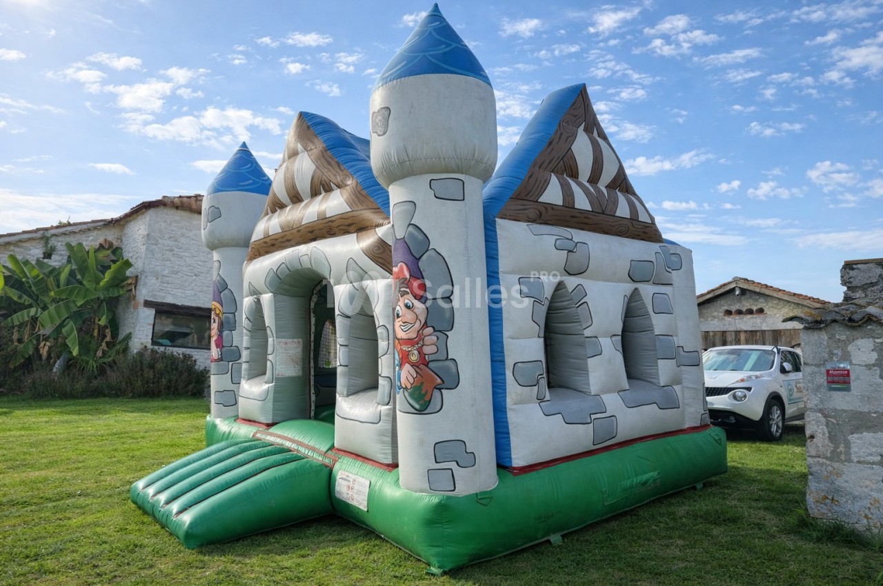 Château gonflable en forme de forteresse médiévale installé sur une pelouse par une journée ensoleillée.