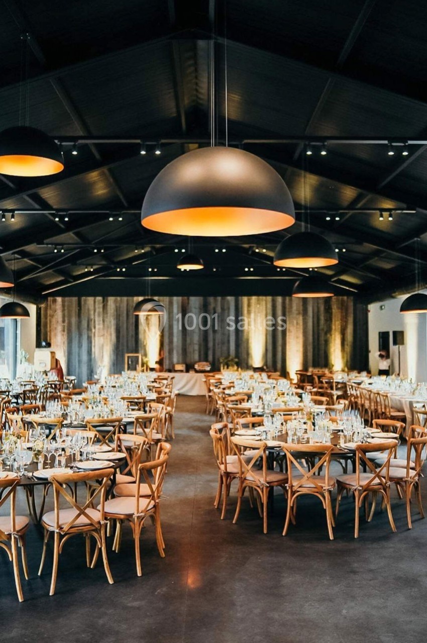 Salle de réception élégamment décorée avec des tables rondes, chaises en bois et éclairage suspendu chaleureux.