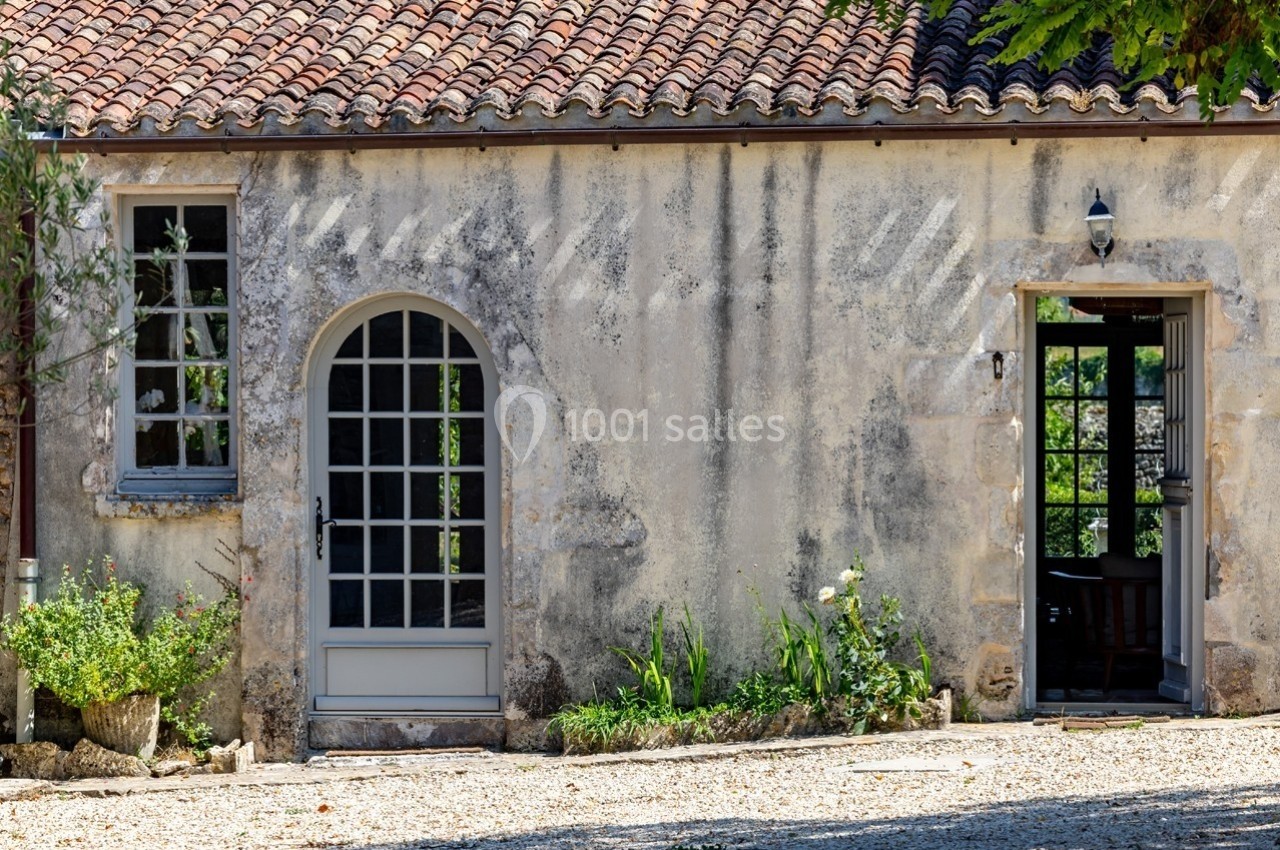 Façade d'une maison en pierre avec deux portes vitrées, des plantes au pied du mur et un sol en gravier.