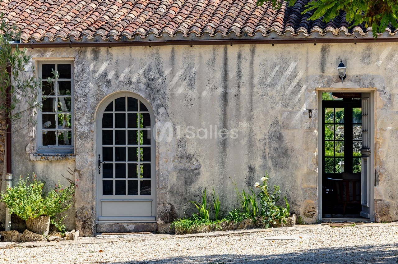 Façade d'une maison en pierre avec portes vitrées, fenêtres et plantes devant un sol en gravier.