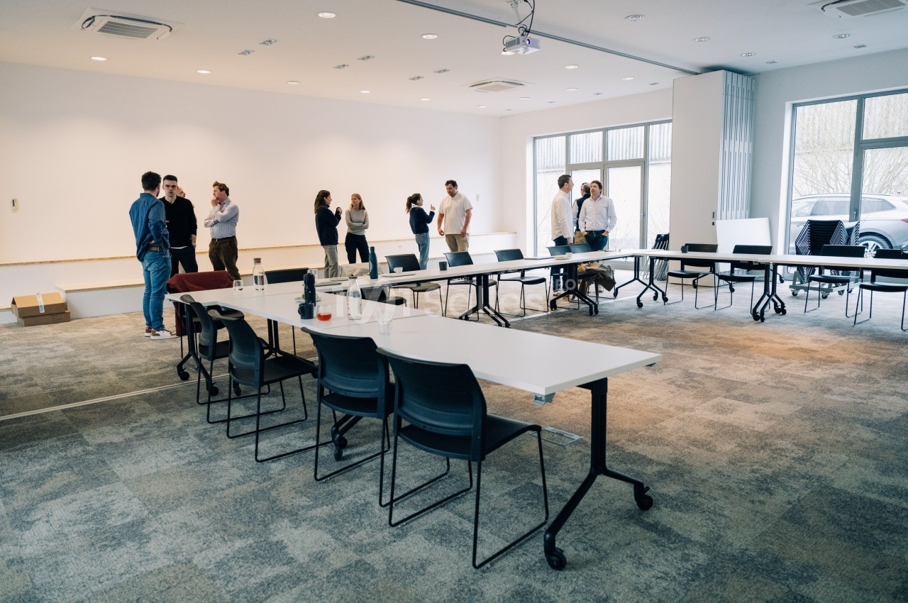 Personnes discutant en petits groupes dans une salle de réunion lumineuse avec des tables et des chaises disposées en U.
