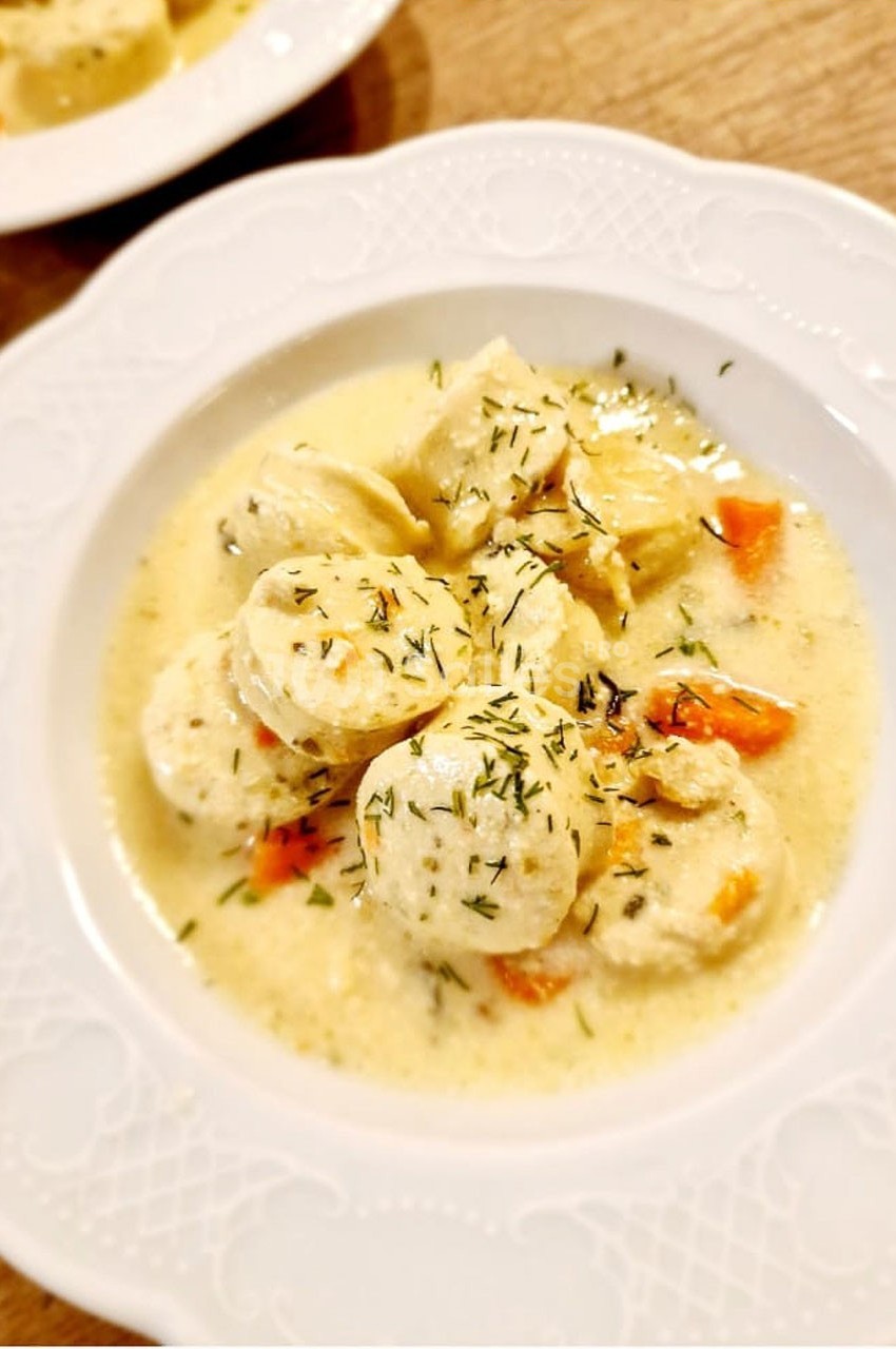 Assiette de quenelles nappées de sauce crémeuse, garnies de carottes et d'herbes, servie sur une table en bois.