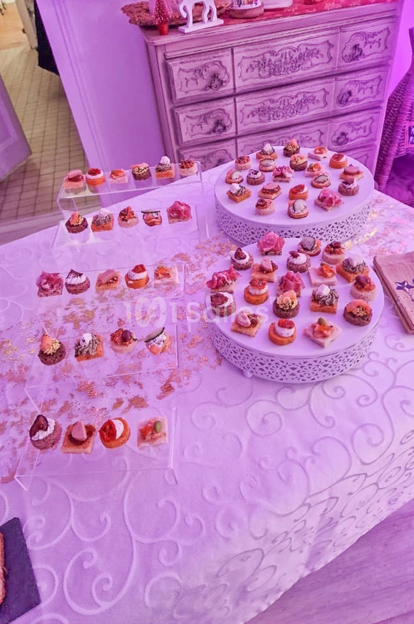Plateau de petits fours variés disposés sur une table blanche décorée, éclairée par une lumière violette.